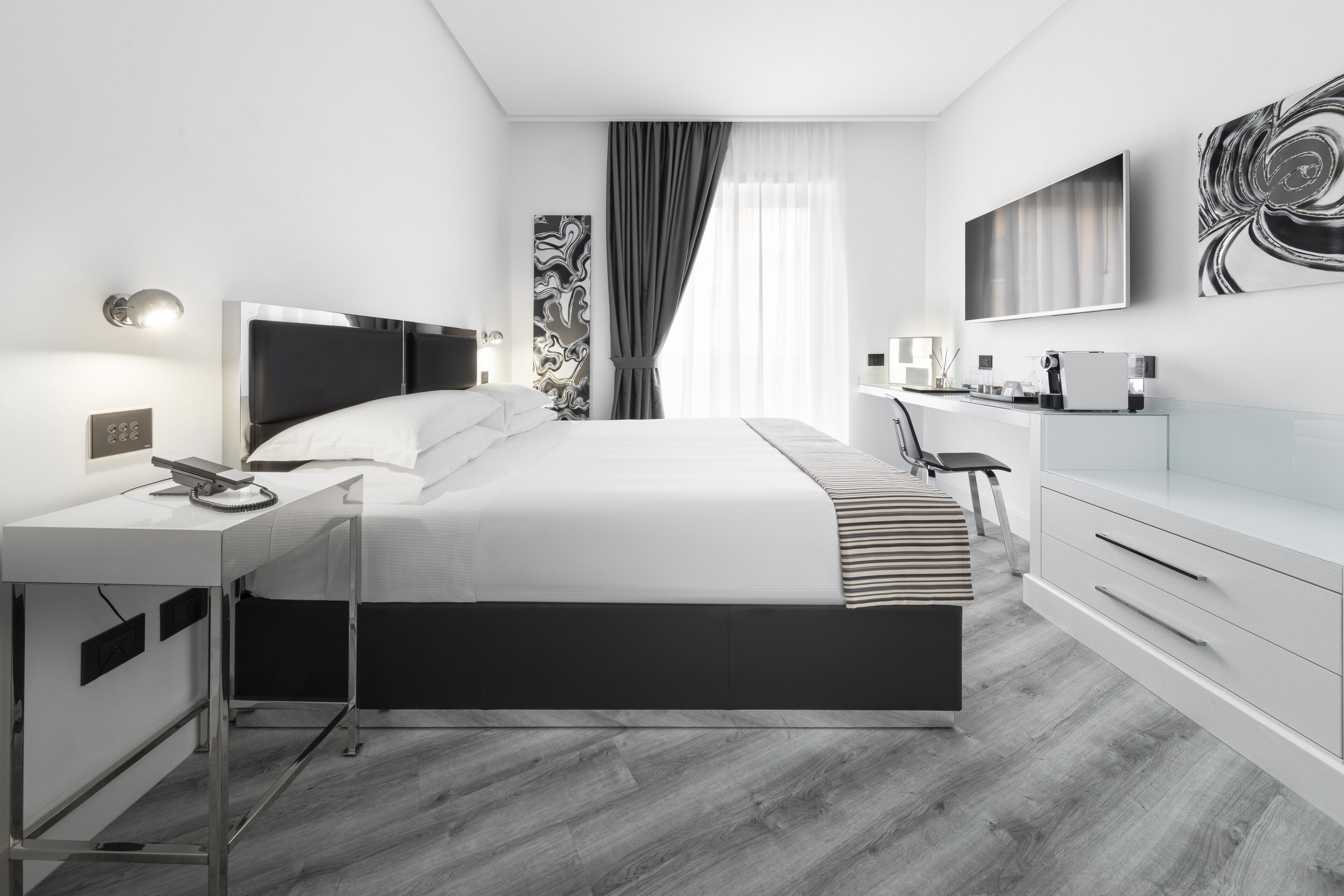 A modern hotel room with a large bed, a desk with a telephone, a flat-screen TV, and a dresser.