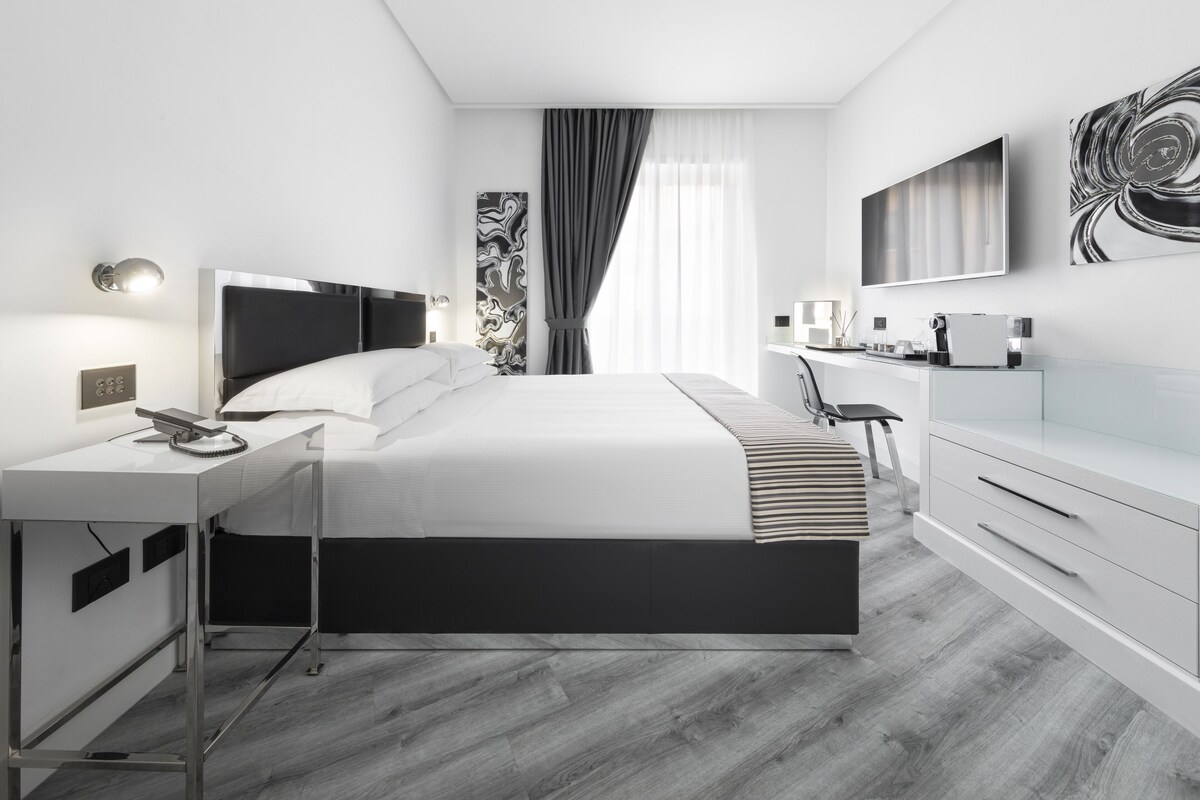 Ein modernes Hotelzimmer mit einem großen Bett, einem Schreibtisch mit Telefon, einem Flachbildfernseher und einer Kommode.