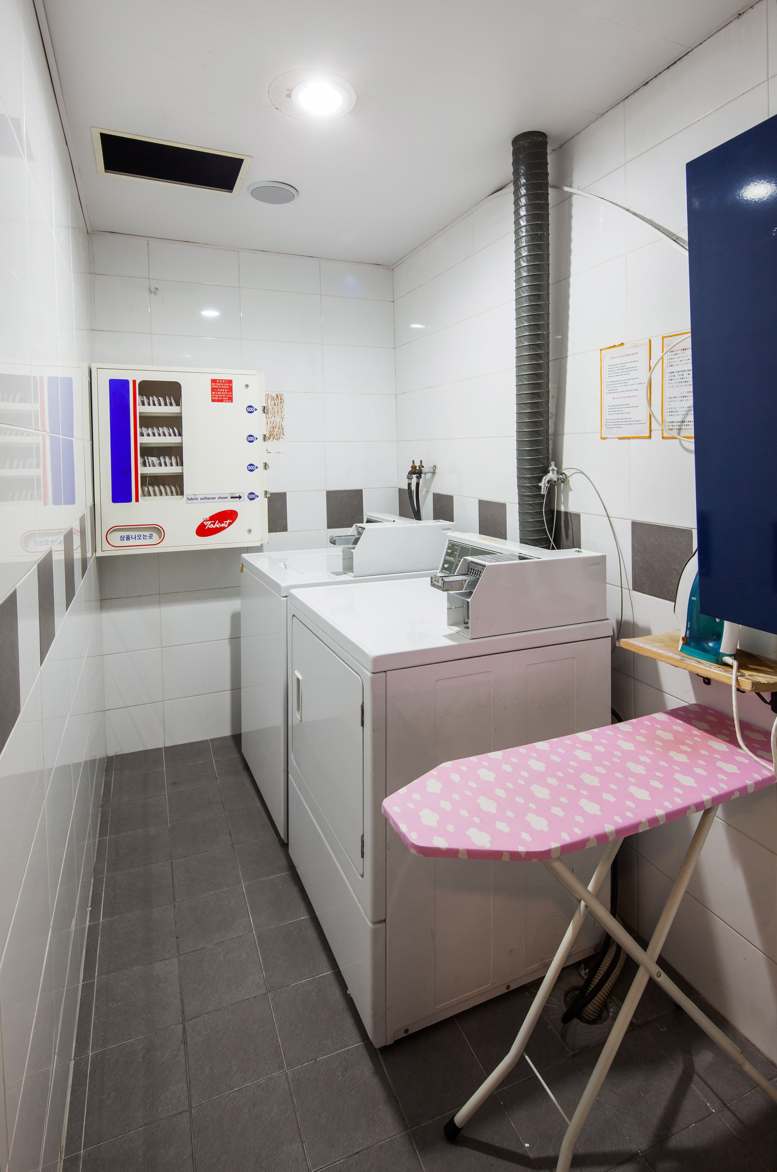 A laundry room with a washing machine, dryer, ironing station, and a control panel.