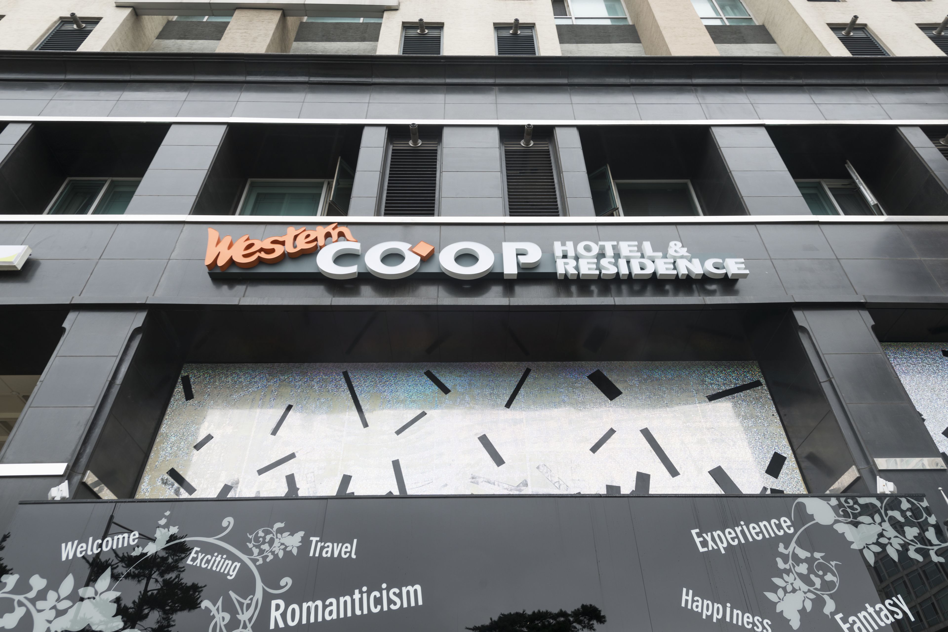 A hotel entrance with the name "Western COOP HOTEL & RESIDENCE" and decorative elements like "Welcome," "Exciting," "Travel," "Romanticism," "Experience," "Happiness," and "Fantasy" on the facade.