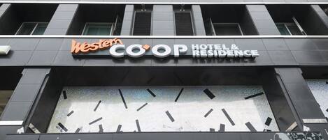 A hotel entrance with the name "Western COOP HOTEL & RESIDENCE" and decorative elements like "Welcome," "Exciting," "Travel," "Romanticism," "Experience," "Happiness," and "Fantasy" on the facade.
