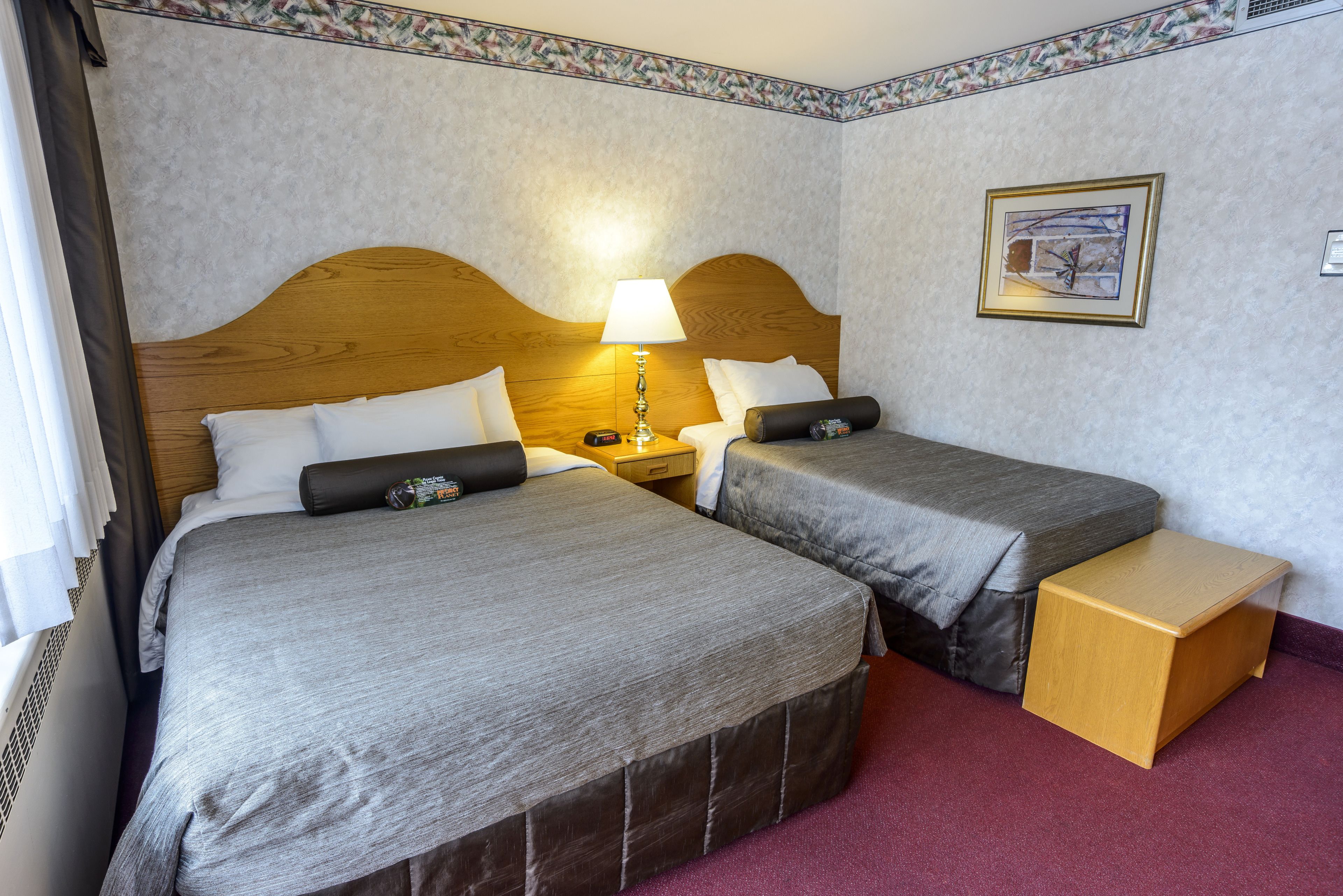 A hotel room with two beds, a nightstand, a lamp, a small wooden table, and a framed picture on the wall.