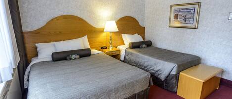 A hotel room with two beds, a nightstand, a lamp, a small wooden table, and a framed picture on the wall.