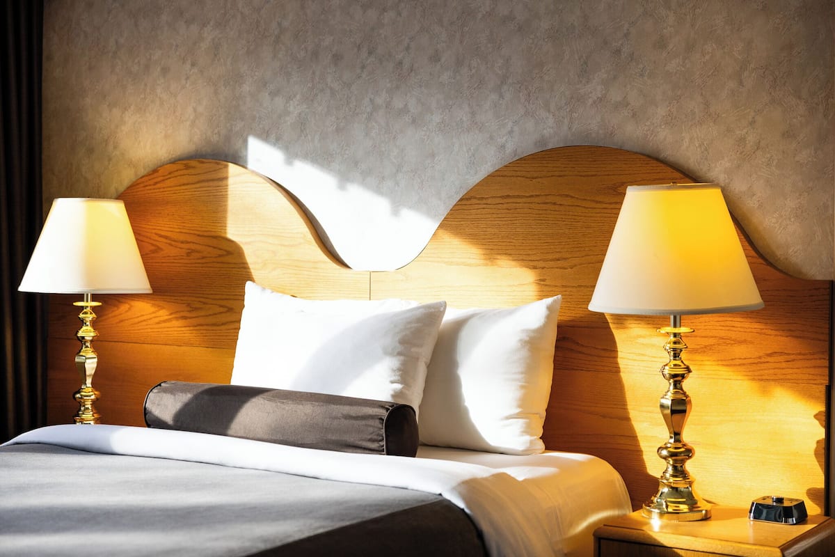 A neatly made bed with white and gray bedding, two bedside lamps, and a wooden headboard.