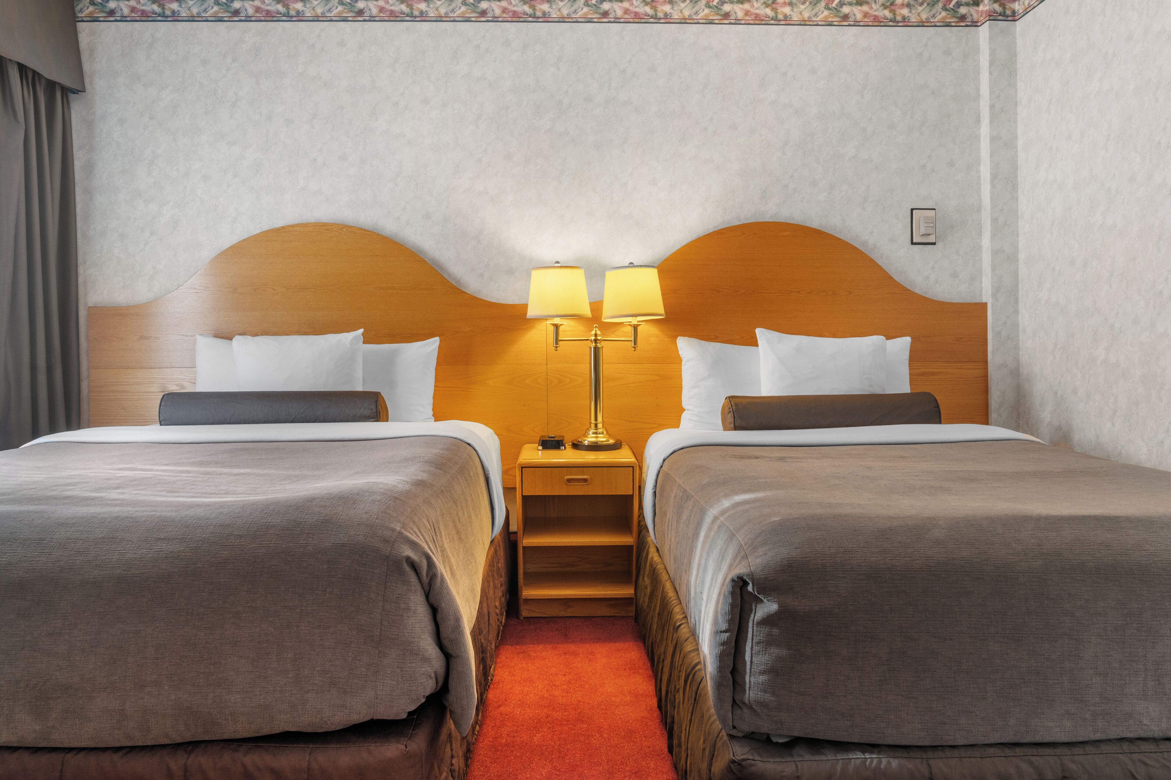 A hotel room with two beds, a nightstand with lamps, and a carpeted floor.