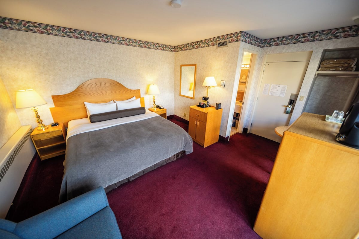 A hotel room with a large bed, two bedside tables with lamps, a wooden nightstand, a desk with a chair, and a mirror on the wall.