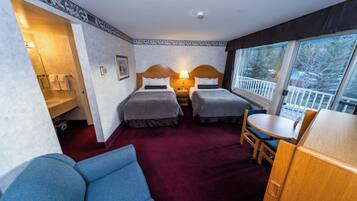 A hotel room with two beds, a sofa, a dining table, and a view of the outdoors.