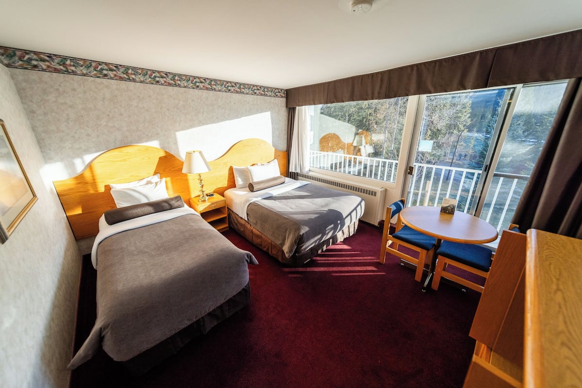 A hotel room with two beds, a small table, and a balcony with a railing.
