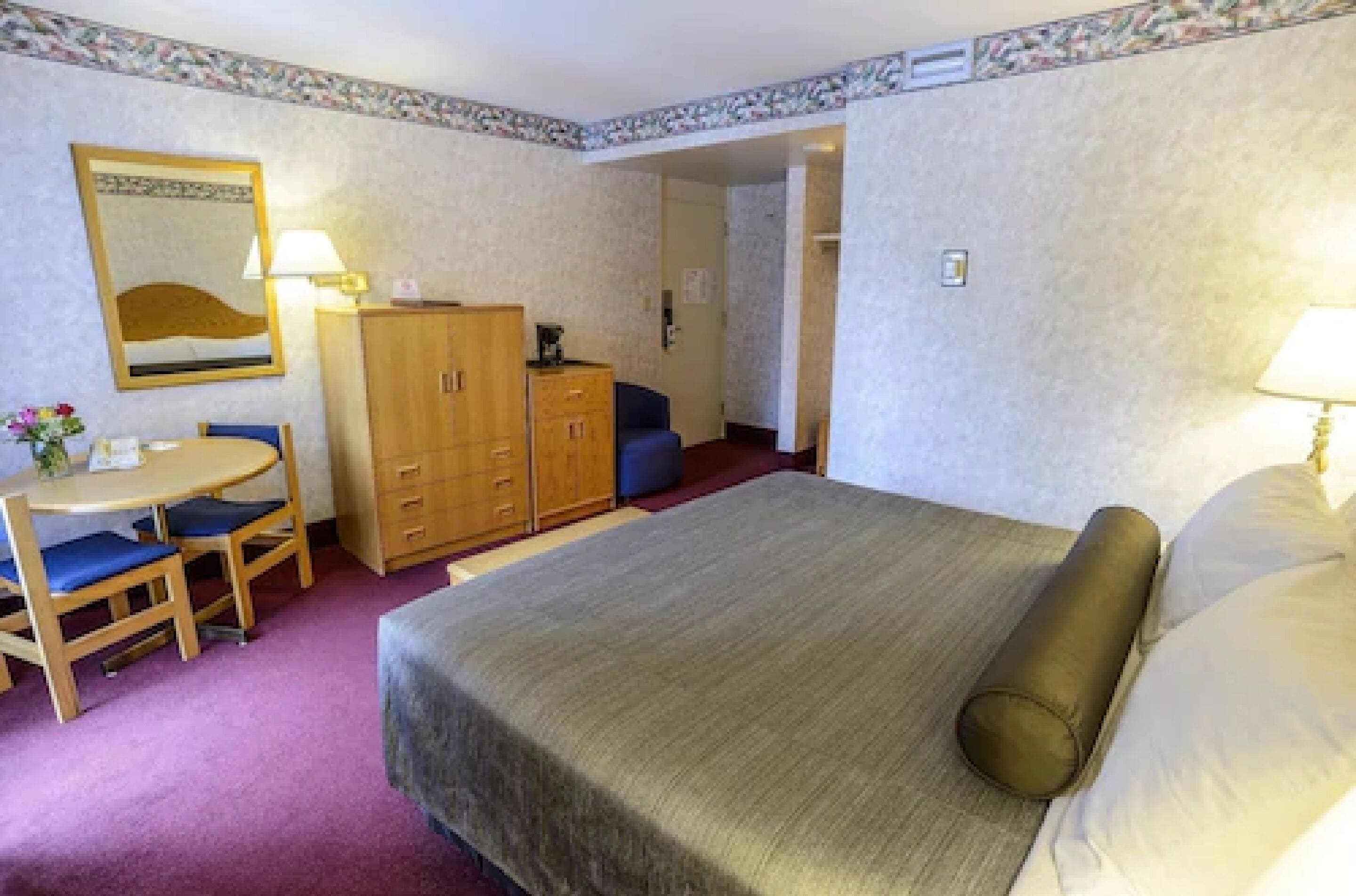 Una habitación de hotel con una cama, un escritorio con una silla, un armario y una lámpara.