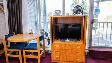 Een gezellig, ruimtelijk interieur met een houten tv-meubel, een flatscreen televisie, een klein tafeltje en blauwe fauteuils.