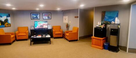 A living room with four orange armchairs, a coffee table, a flat-screen TV, and a refrigerator.
