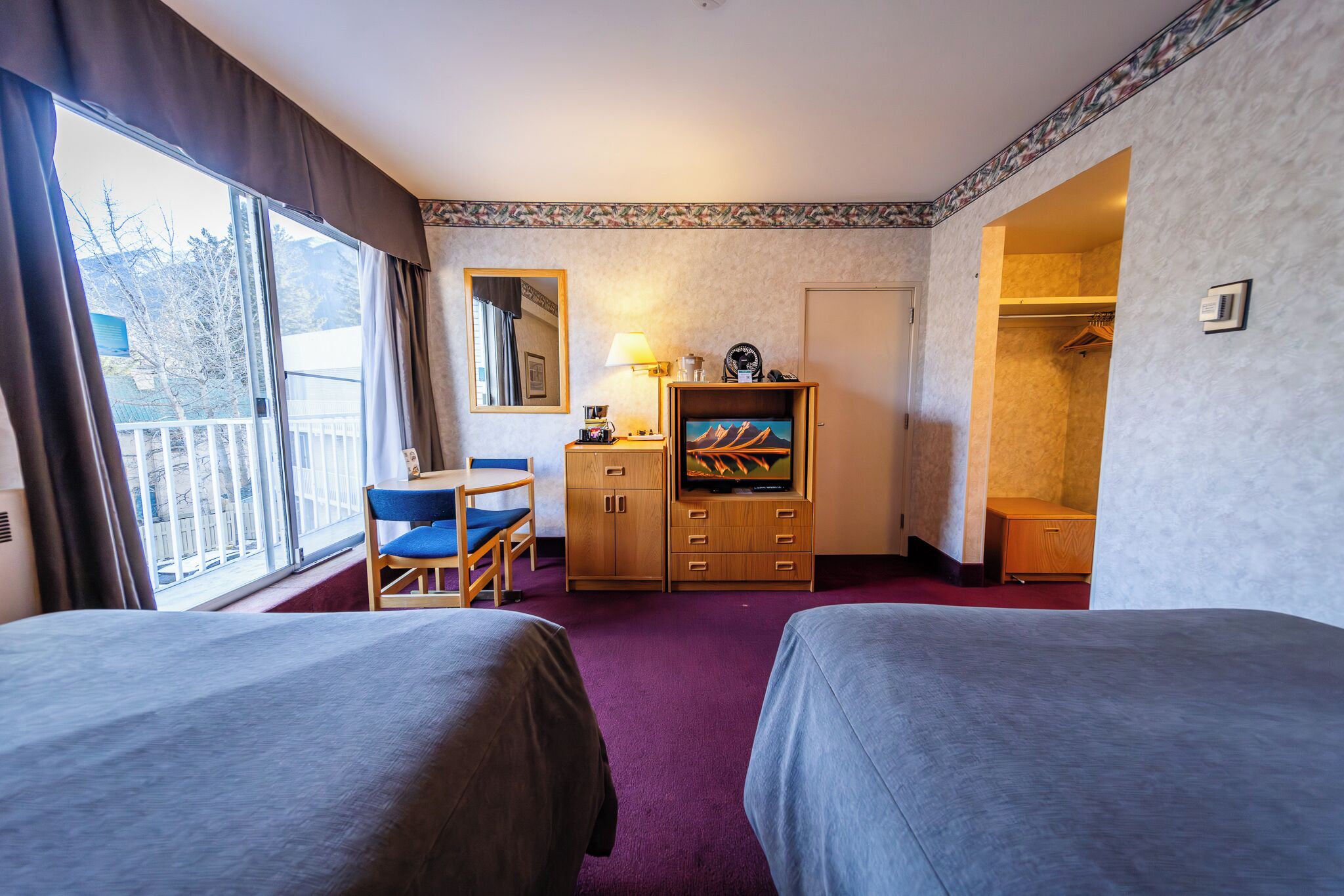 A hotel room with two beds, a desk with a chair, a TV, a wardrobe, and a window with curtains.