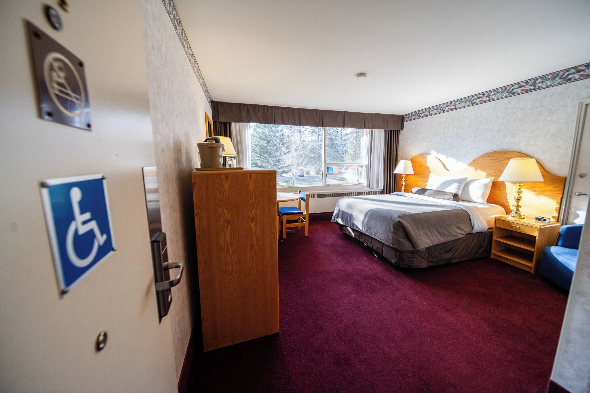 A hotel room with a bed, a desk, a chair, and a window with a view of trees.