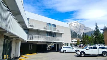 Un immeuble à plusieurs étages doté de balcons, d’un espace de stationnement et surplombant un paysage montagneux.