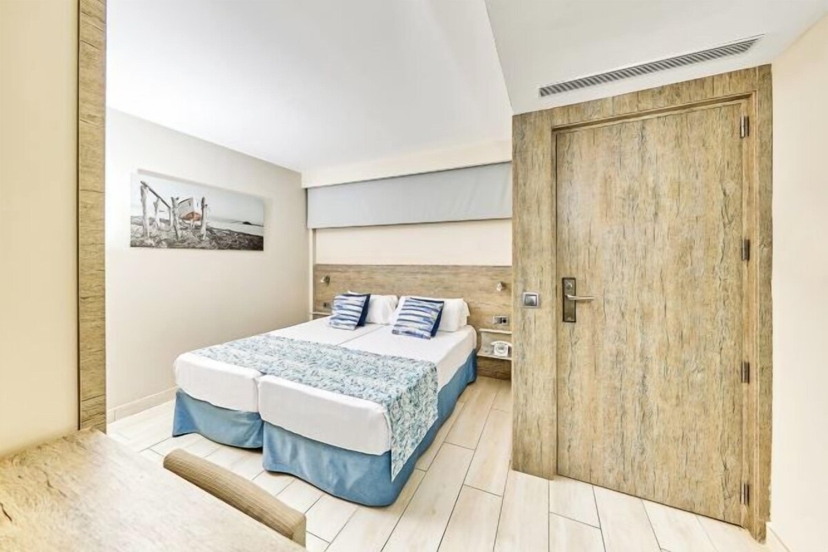 A bedroom with a bed, a wooden door, a nightstand, and a picture on the wall.