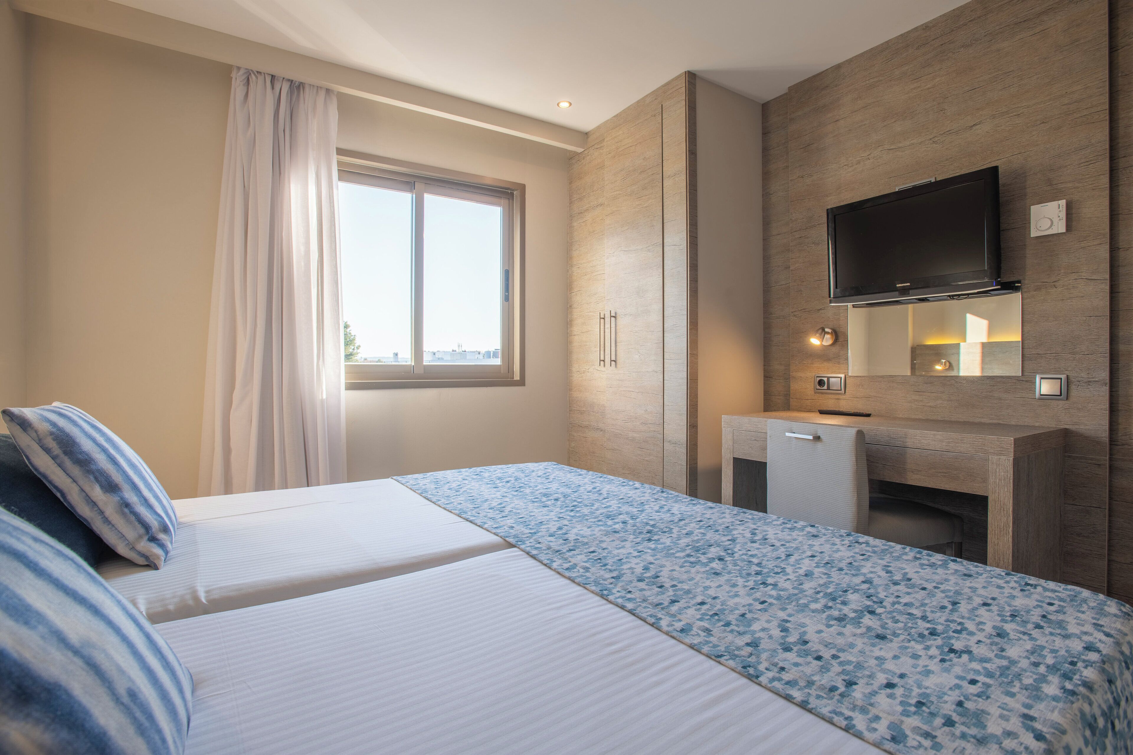A hotel room with a bed, a desk, a TV, and a window with curtains.