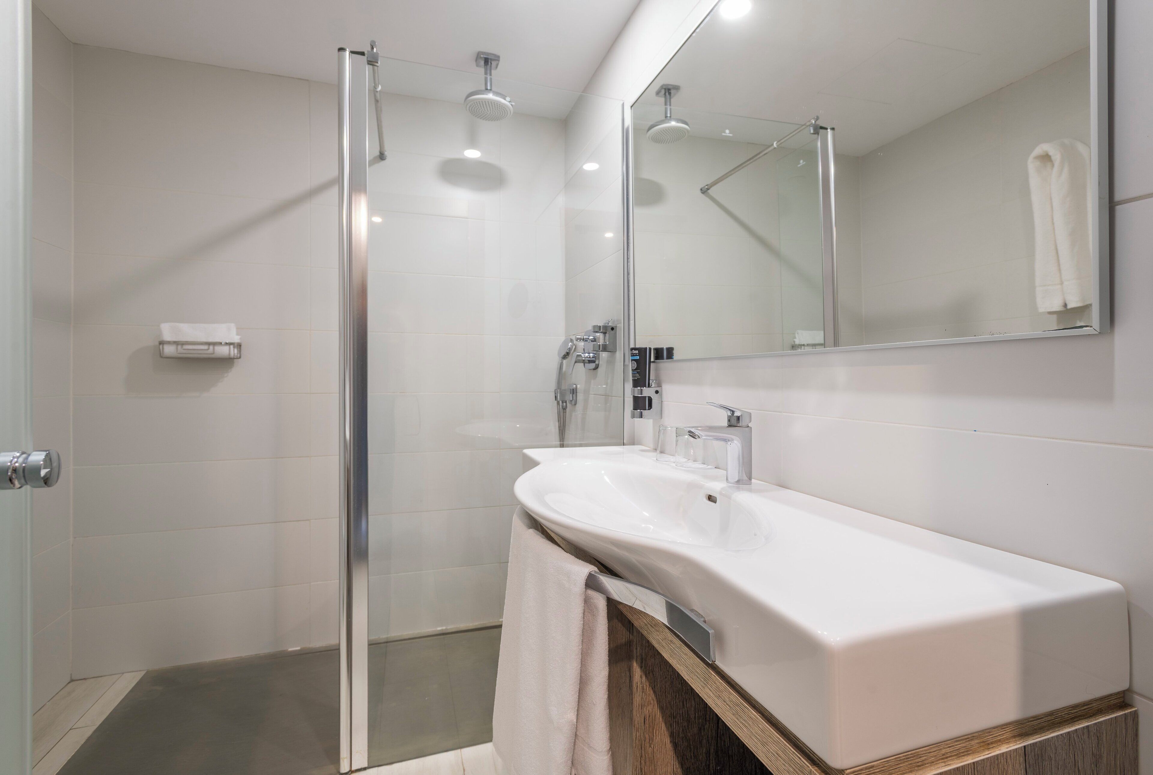 A modern bathroom with a glass shower enclosure, a white sink, and a large mirror.