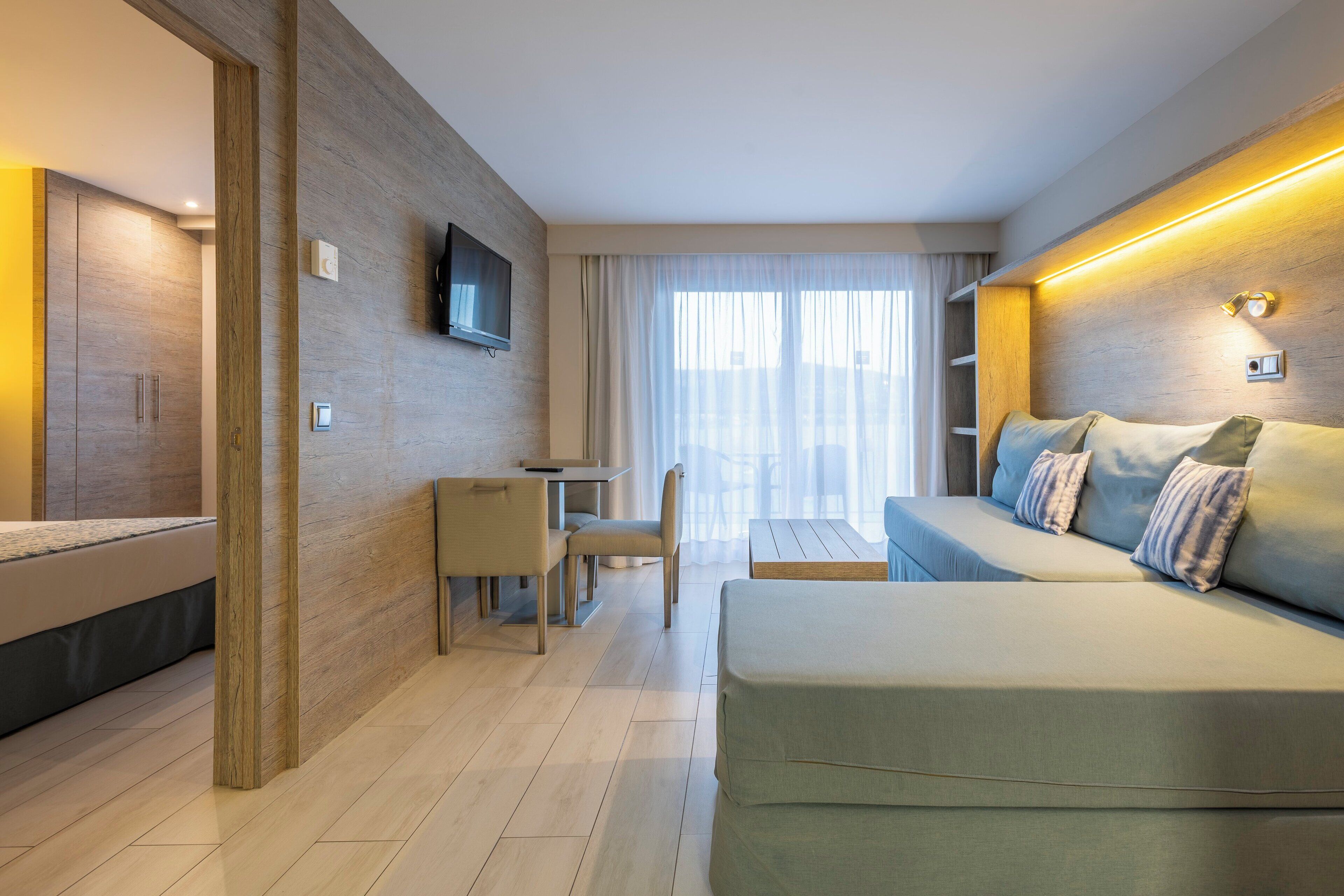 Una habitación de hotel moderna con sofá, escritorio y televisor montado en la pared.