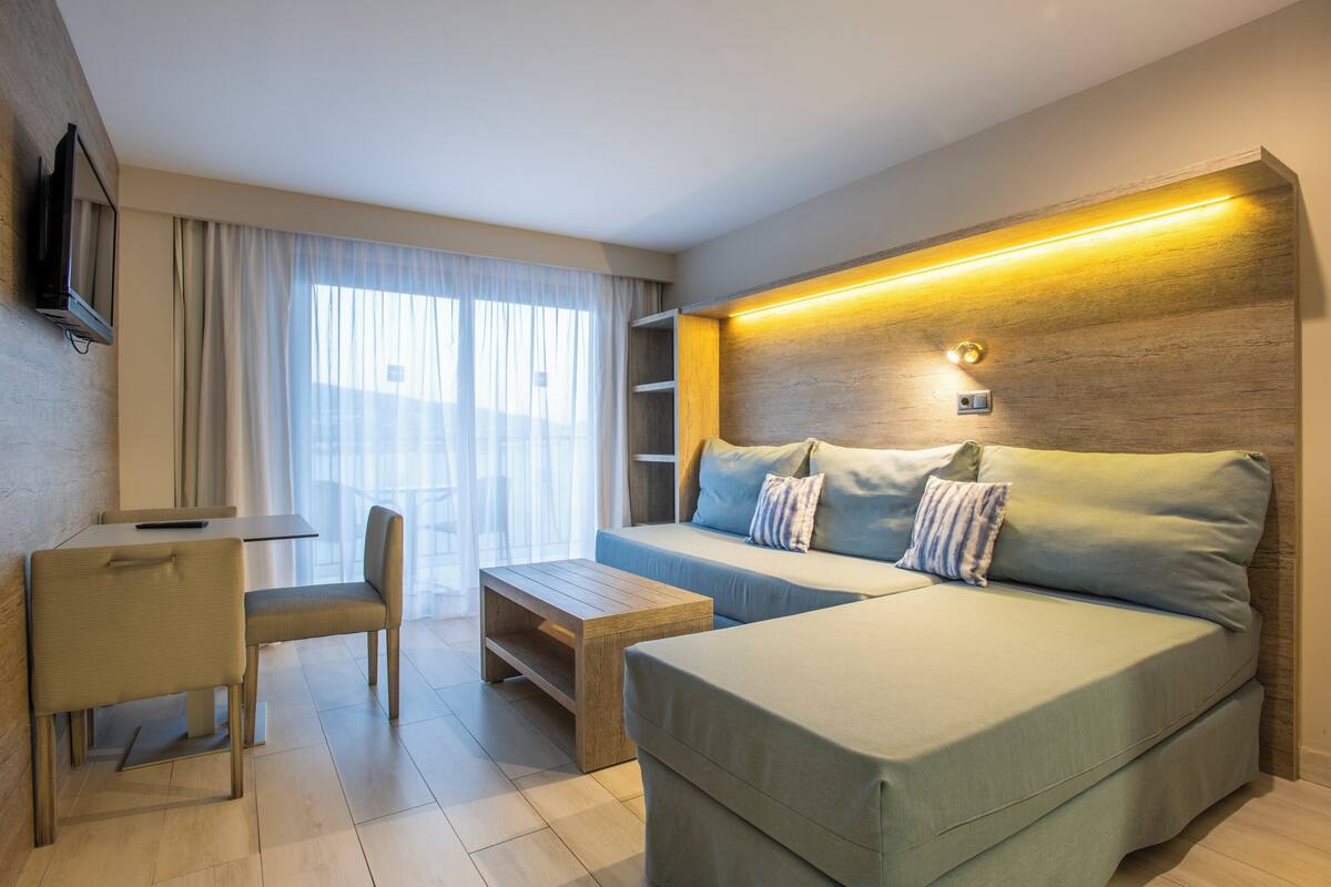 A modern hotel room with a sofa, a chair, a small table, and a TV mounted on the wall.