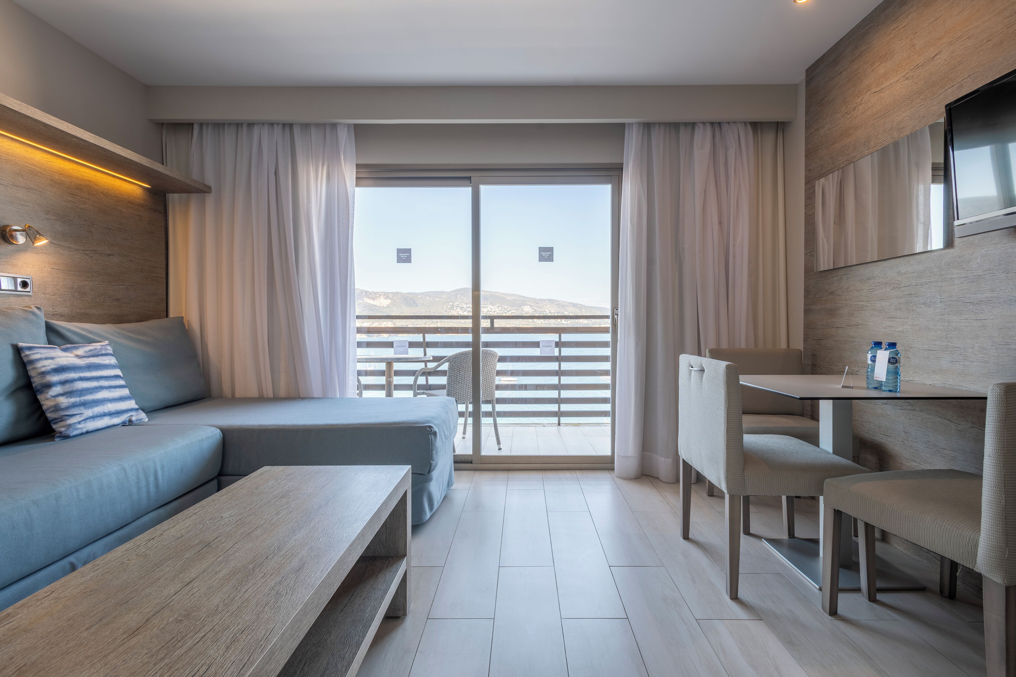 A modern hotel room with a sofa, a dining table, and a balcony with a view.