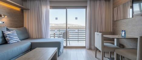 A modern hotel room with a sofa, a dining table, and a balcony with a view.