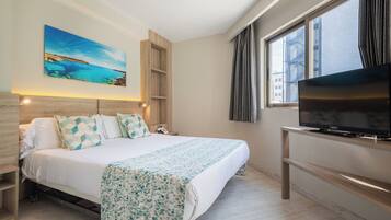 Una habitación de hotel moderna con una cama grande, un televisor sobre un soporte de madera, un cuadro en la pared y una ventana con cortinas.