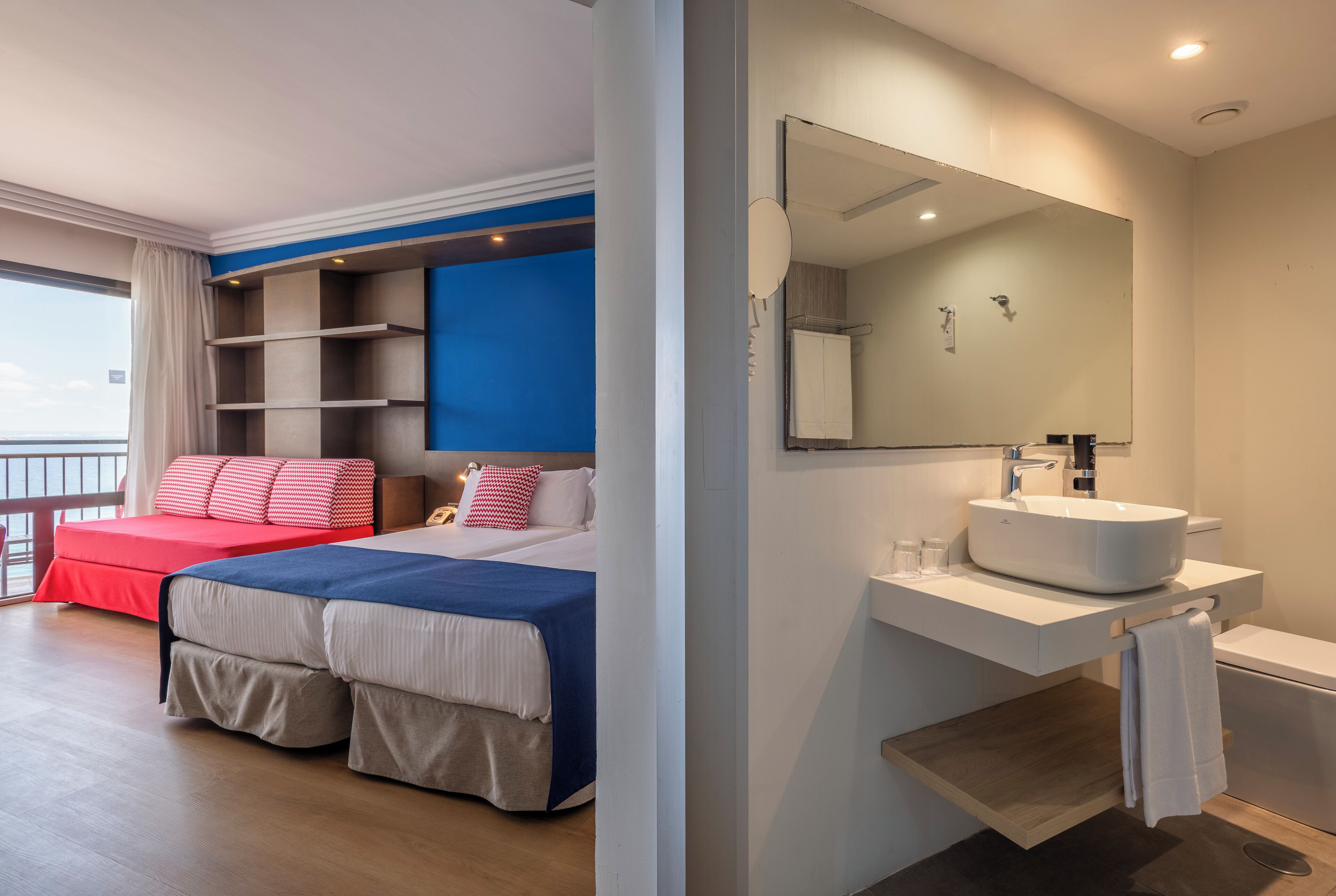 Camera d'albergo moderna con un letto grande, un balcone, un bagno con uno specchio ampio e un lavandino bianco.