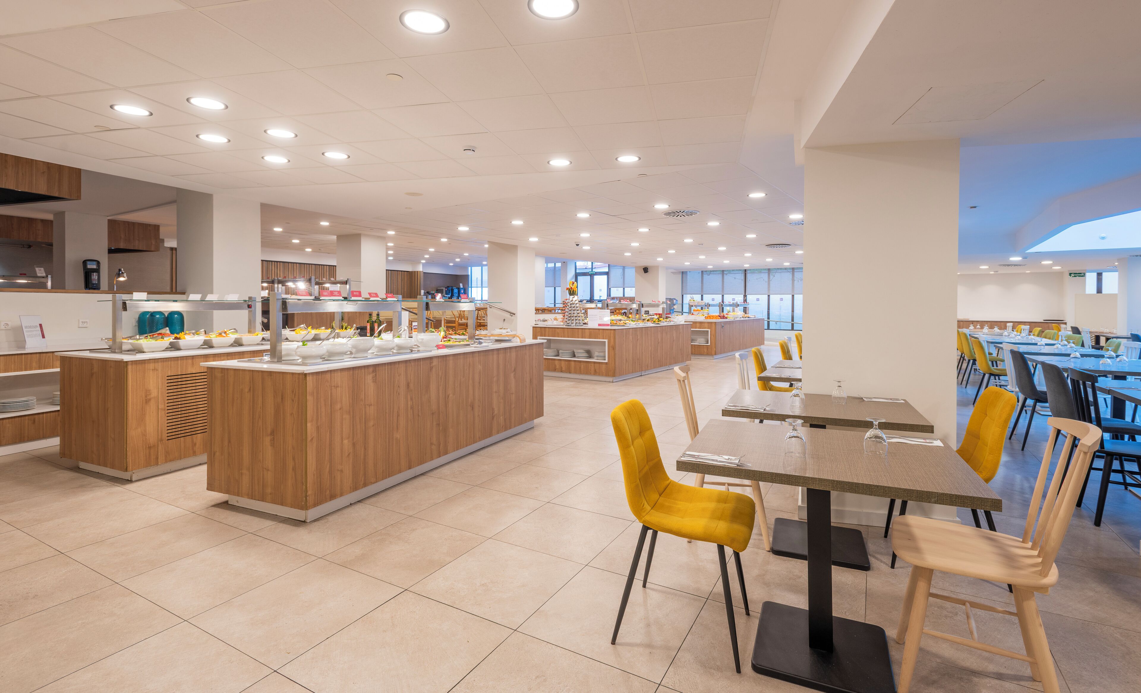 A modern cafeteria with multiple dining areas, a central serving station, and a bright, well-lit environment.