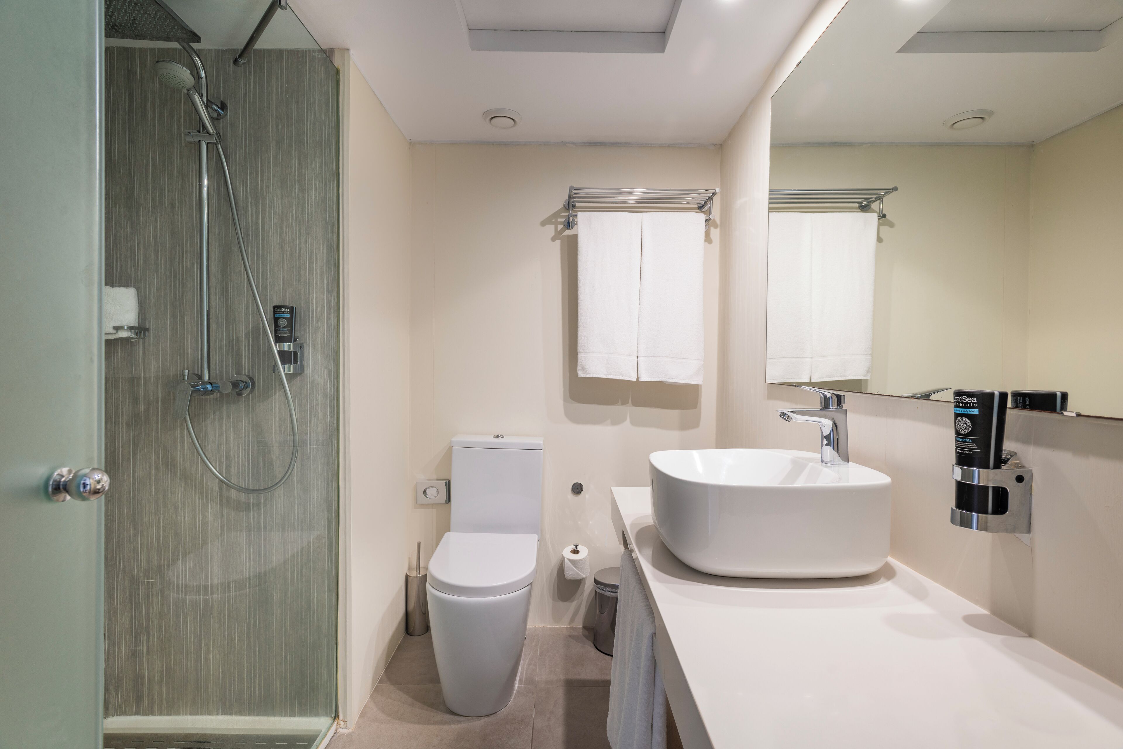 Un baño moderno con ducha de mampara de vidrio, inodoro blanco, lavamanos grande en blanco y un espejo sobre el lavamanos.