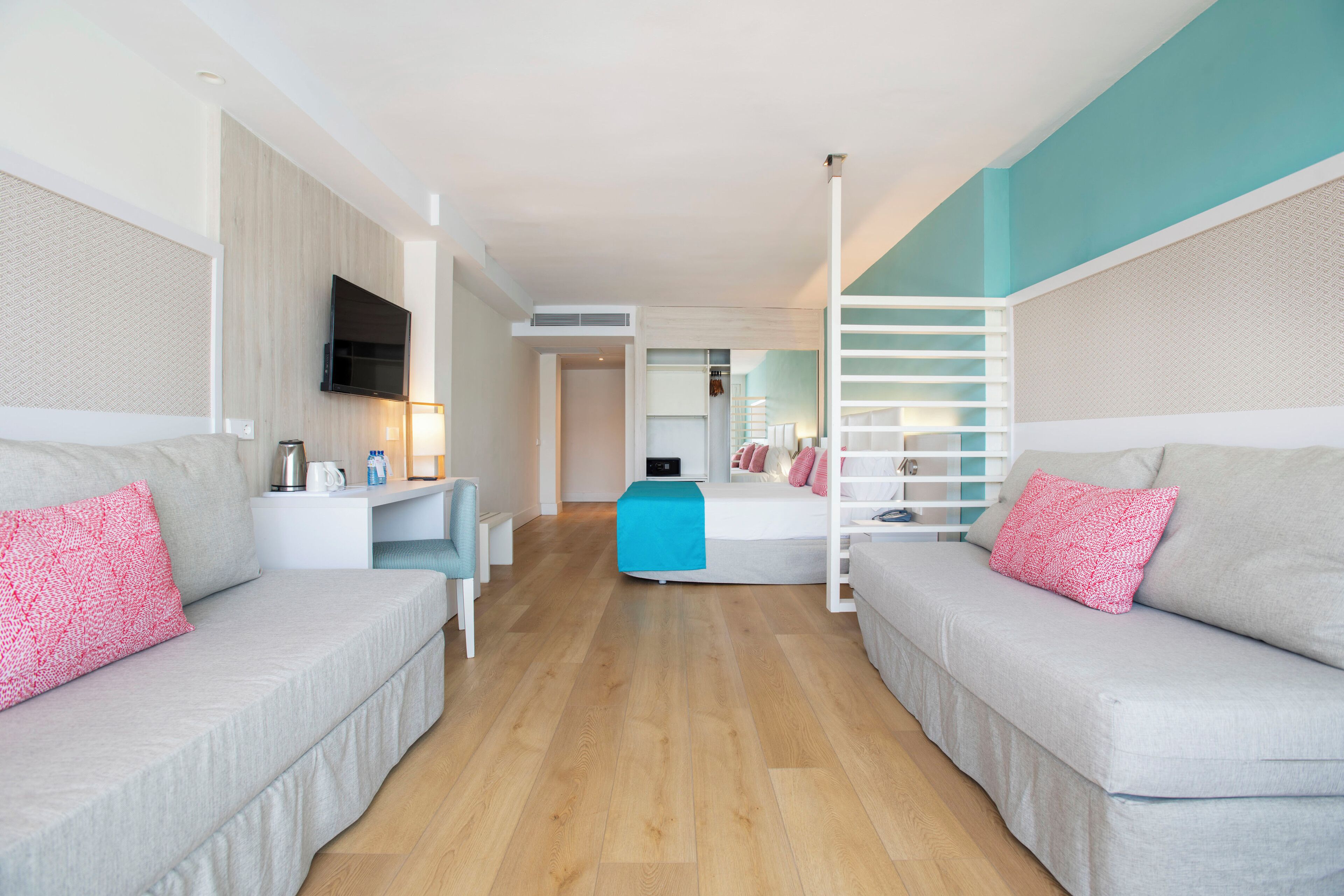 A modern hotel room with two sofas, a TV, and a staircase.