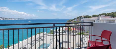 Un balcón con sillas rojas que da a una piscina y una vista despejada del mar.