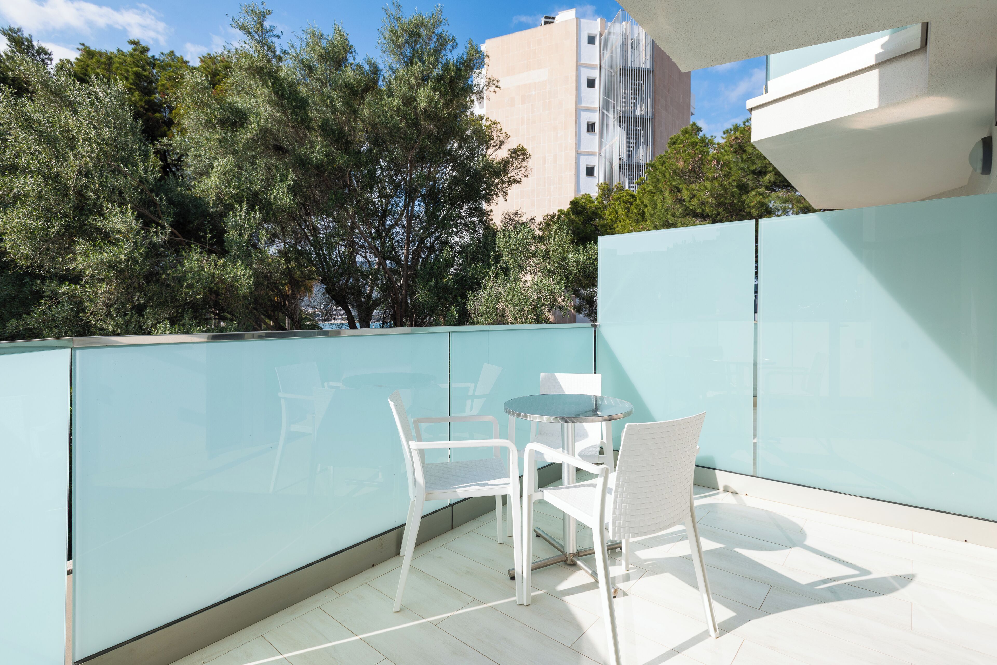 Ein Balkon mit Glastrennwand, weißen Stühlen und einem kleinen Tisch.