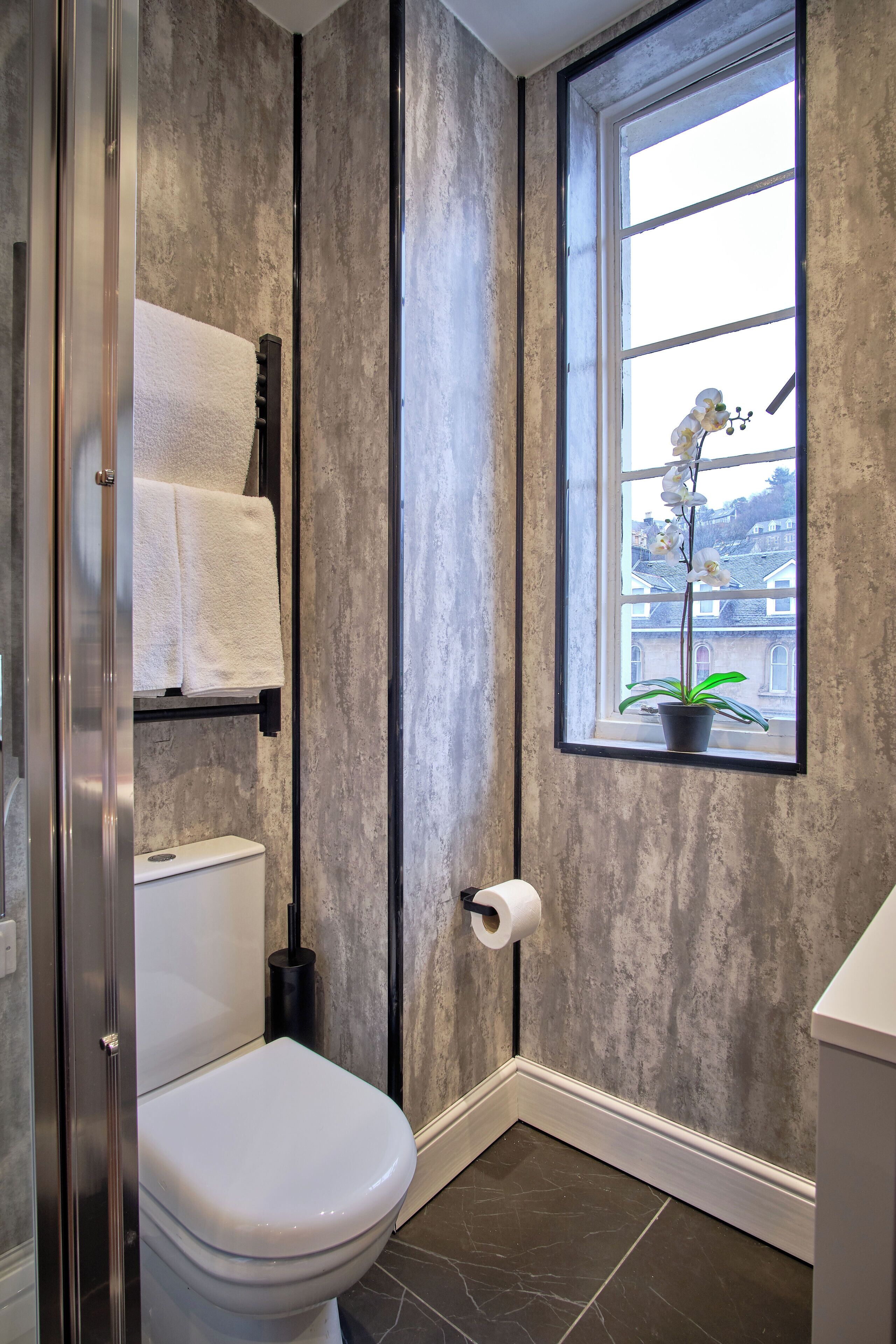 Et badeværelse med toilet, håndklæderække og et vindue med en potteplante.