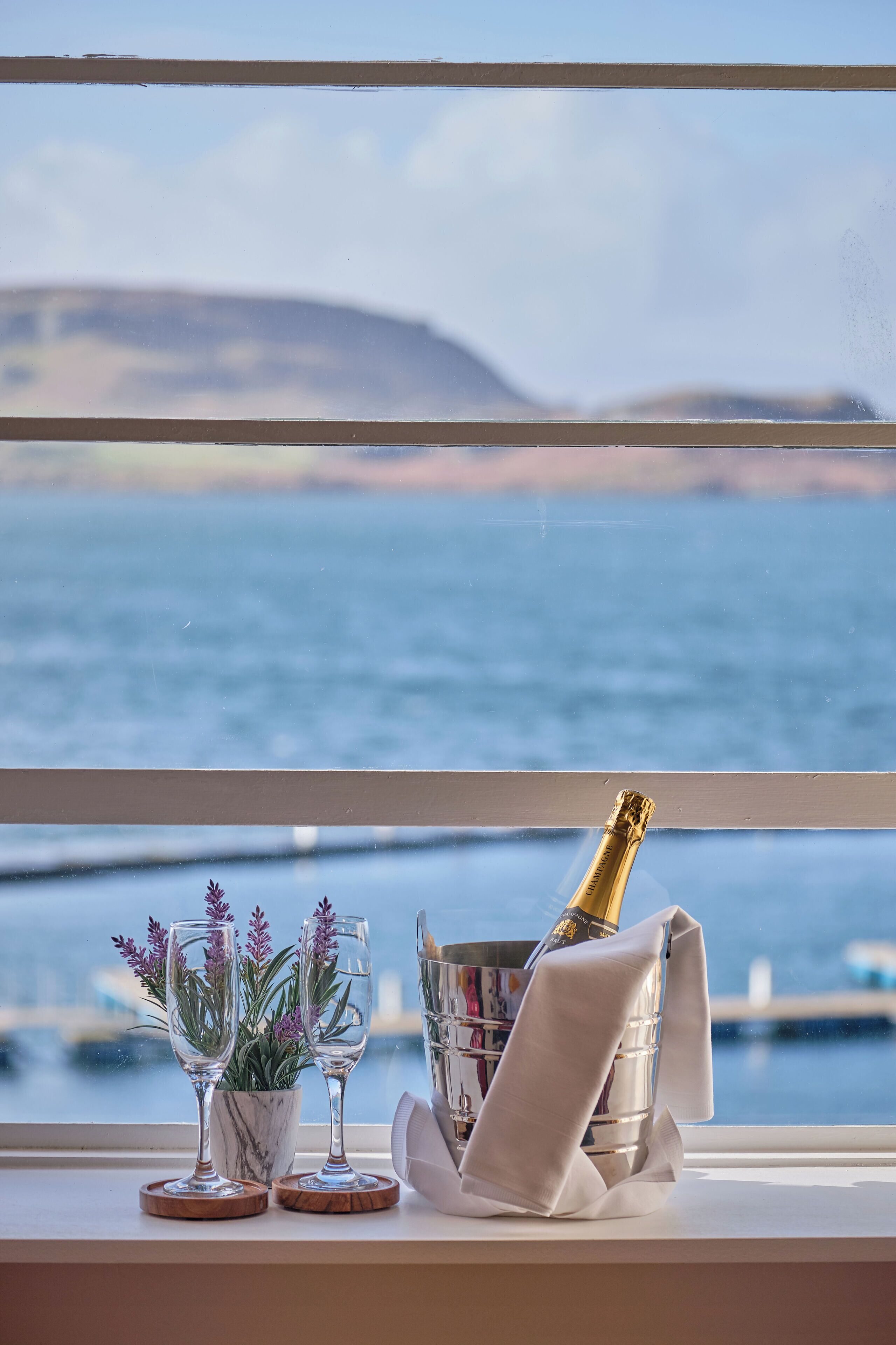 Una ventana con vista al mar, una botella de champán y dos copas sobre el alféizar.