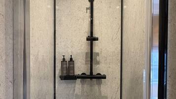 A modern shower enclosure with a glass door, a handheld showerhead, and a shelf with toiletries.