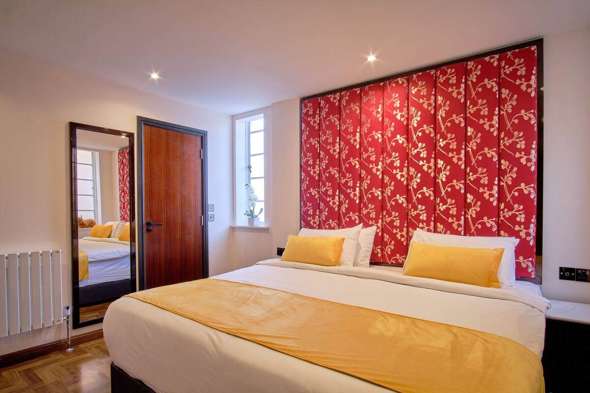 A hotel room with a large bed, a red floral headboard, and a view of the hallway.