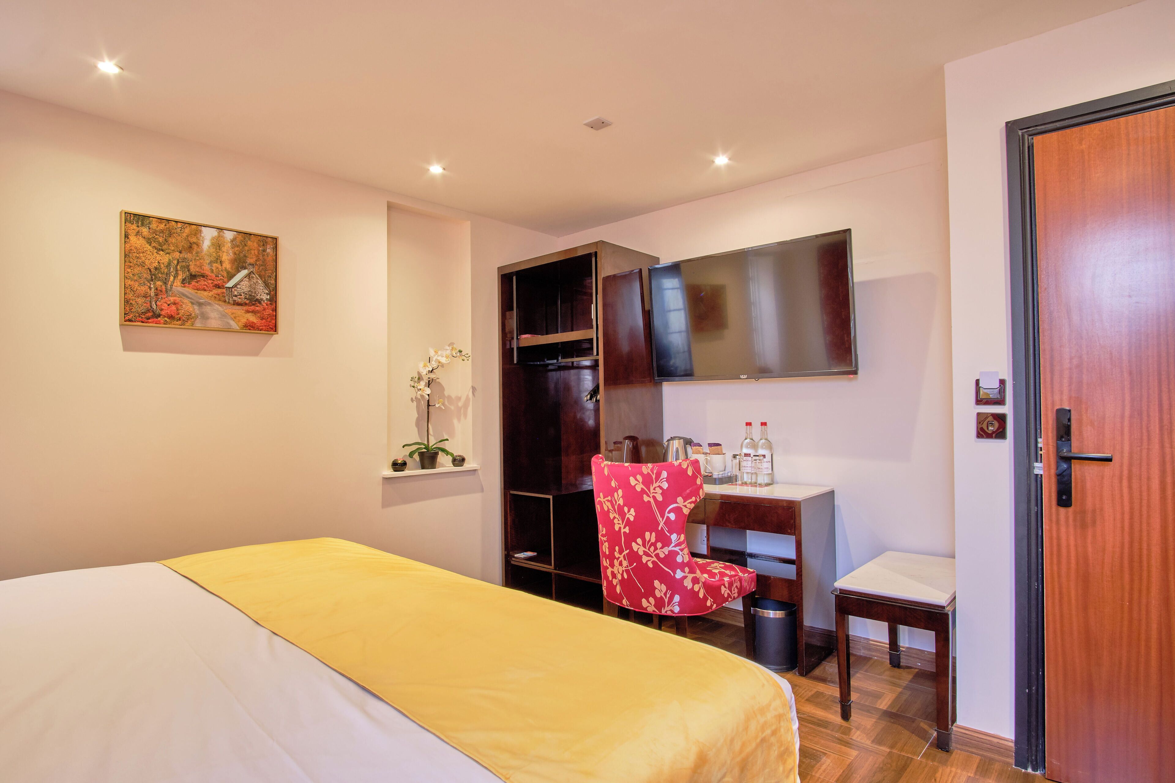 A hotel room with a bed, a desk, a chair, a TV, and a door.