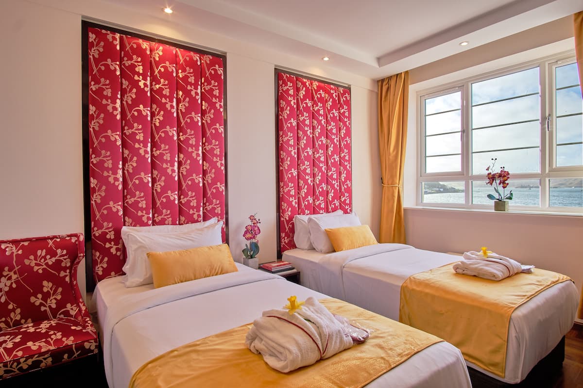 A hotel room with two beds, floral curtains, a window with a view, and a small table with a plant.