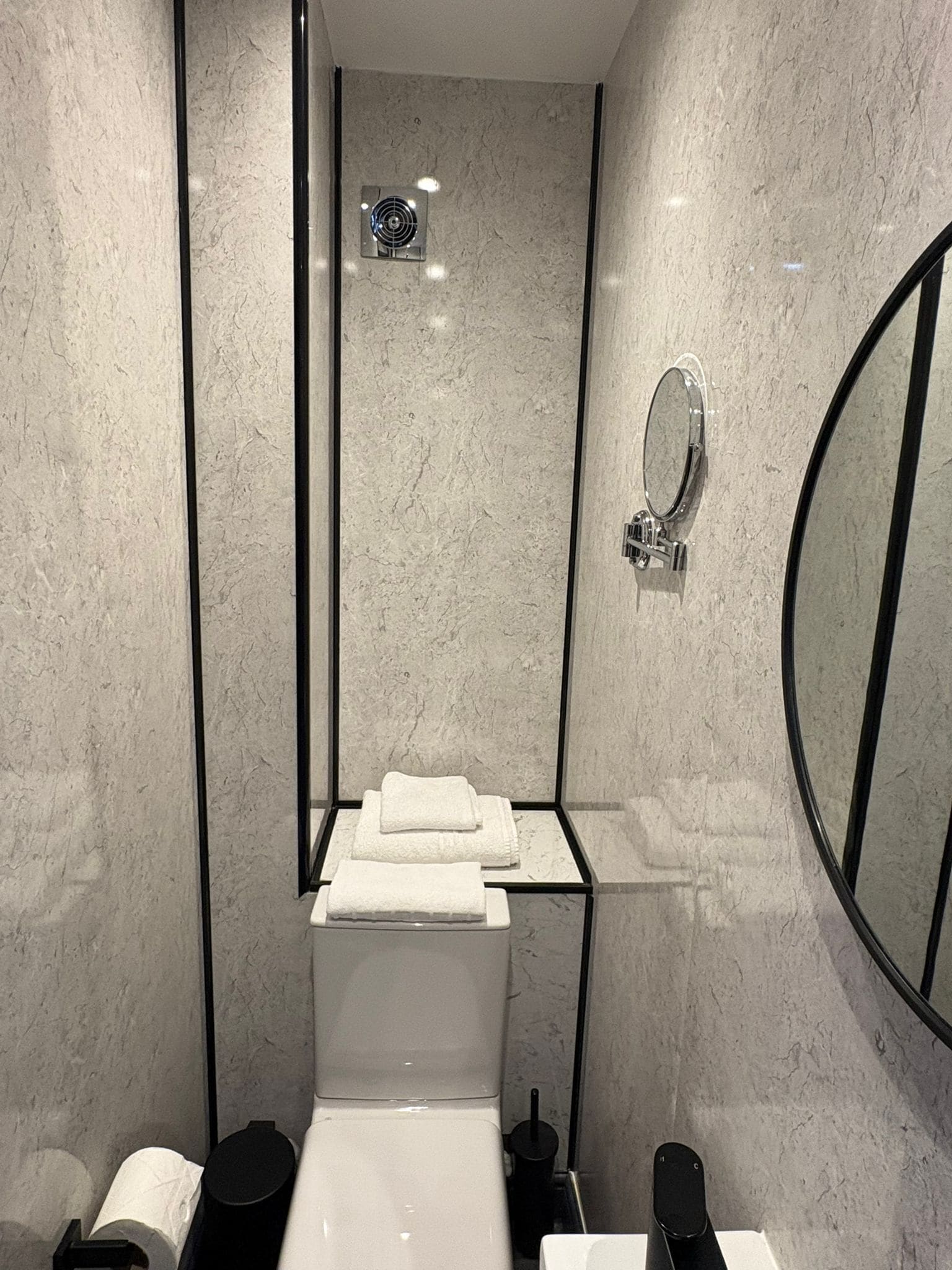 A modern bathroom with a glass partition, a toilet, a sink, a mirror, and a towel rack.