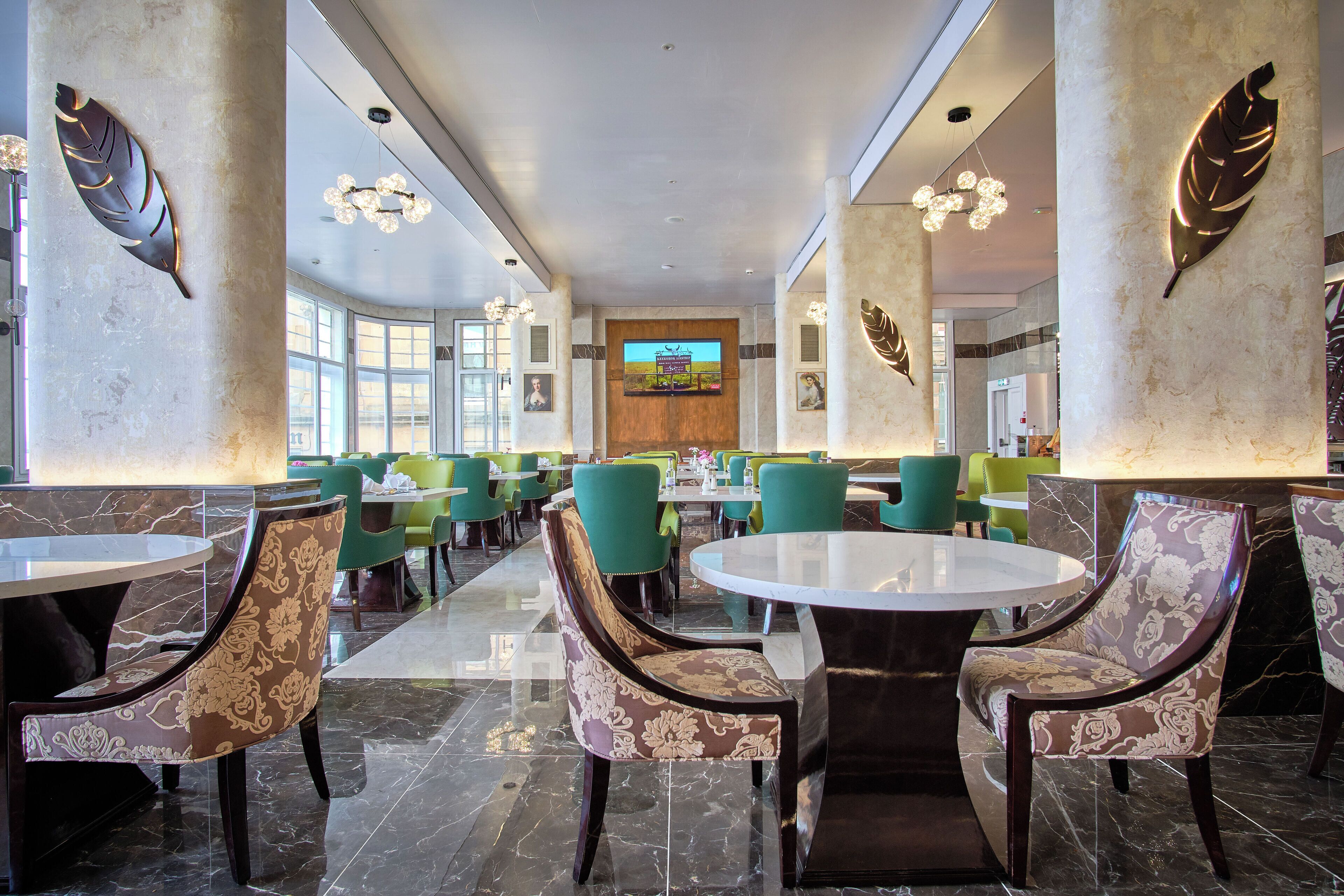 A spacious lobby with high ceilings, large windows, and a central TV screen.