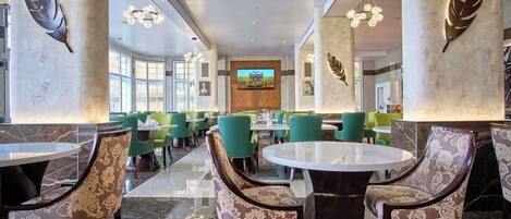 A spacious lobby with high ceilings, large windows, and a central TV screen.