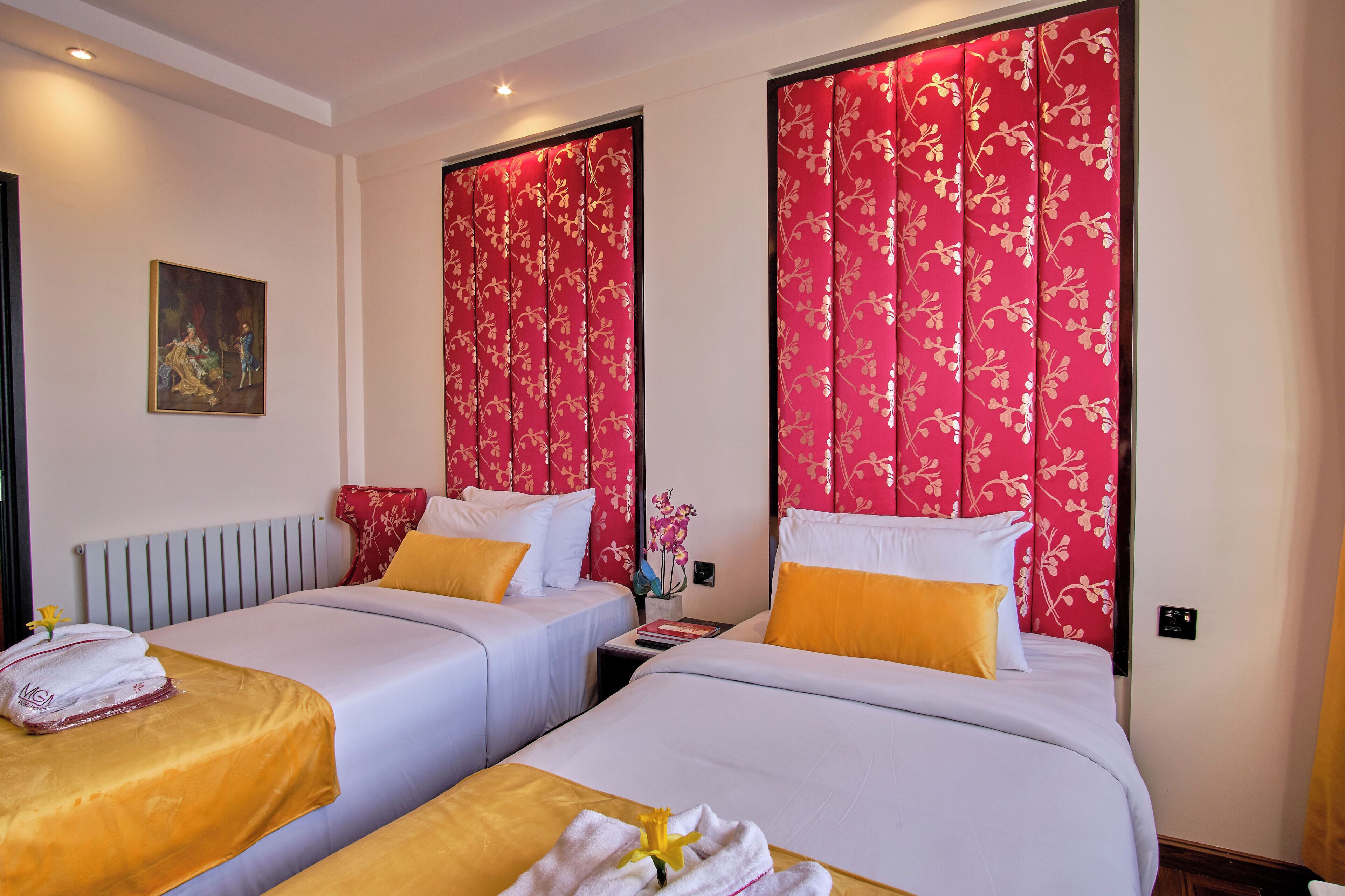 Una habitación de hotel con dos camas, cada una con sábanas blancas y almohadas amarillas, y cortinas florales rojas.