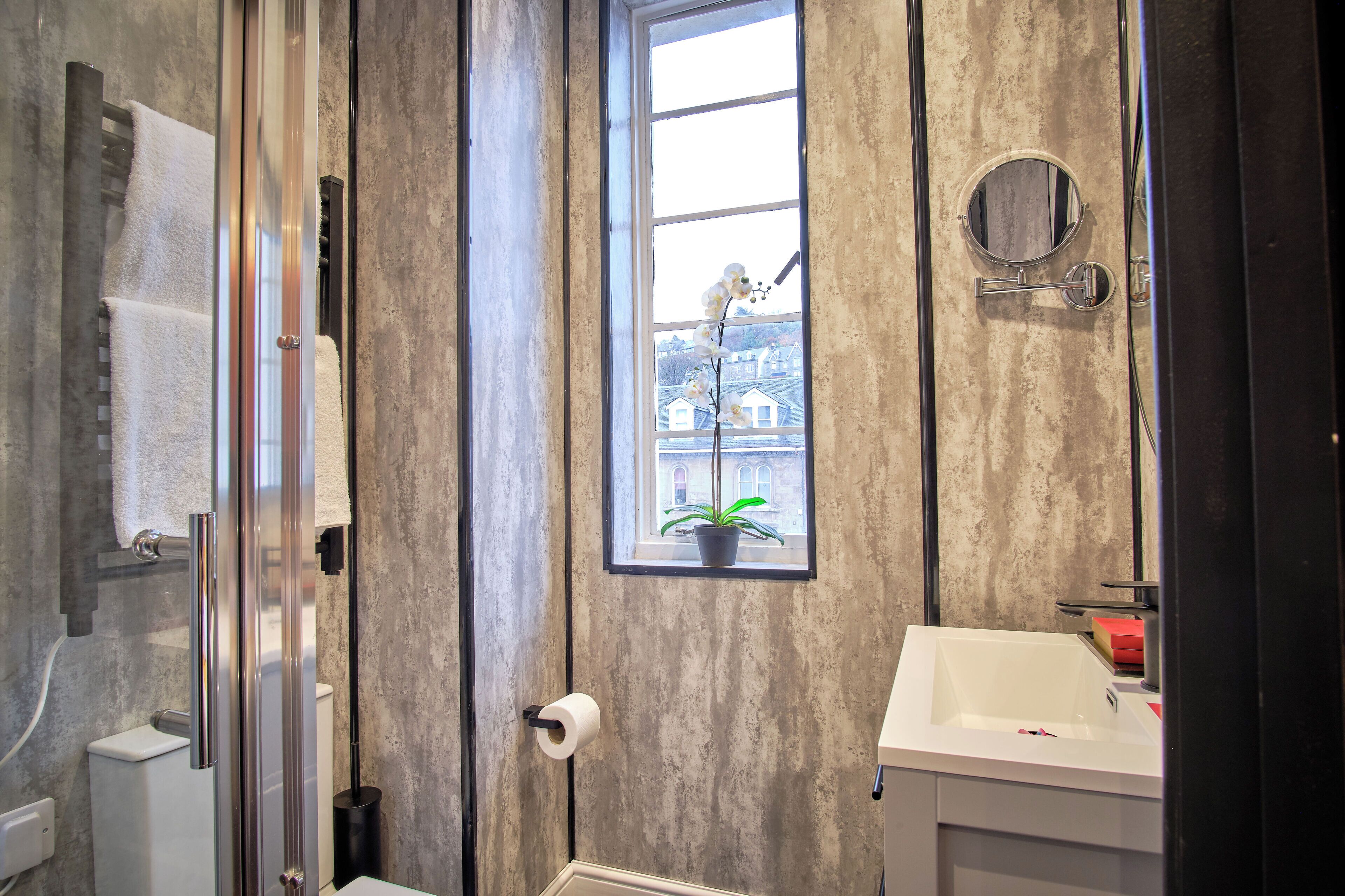 A bathroom with a large window, a towel rack, a toilet, and a sink.