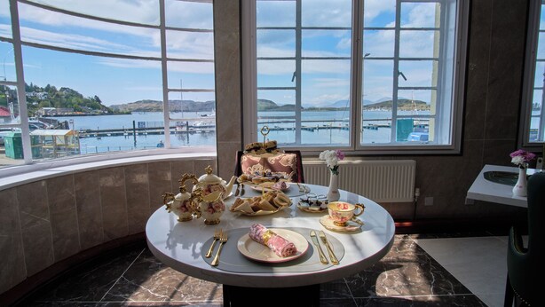 A dining table with a view of a harbor, a vase with flowers, and a chair.