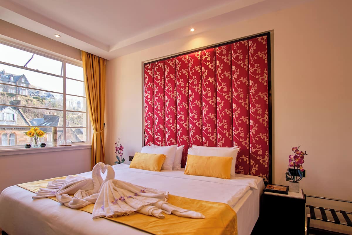 A hotel room with a bed, a window with curtains, and a view of buildings outside.