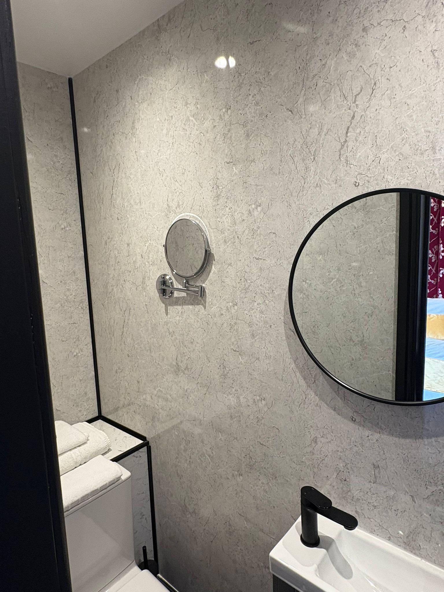 Een badkamer met een marmeren wand, een ronde spiegel, een toilet en een wastafel met een zwarte kraan.