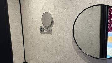 Een badkamer met een marmeren wand, een ronde spiegel, een toilet en een wastafel met een zwarte kraan.