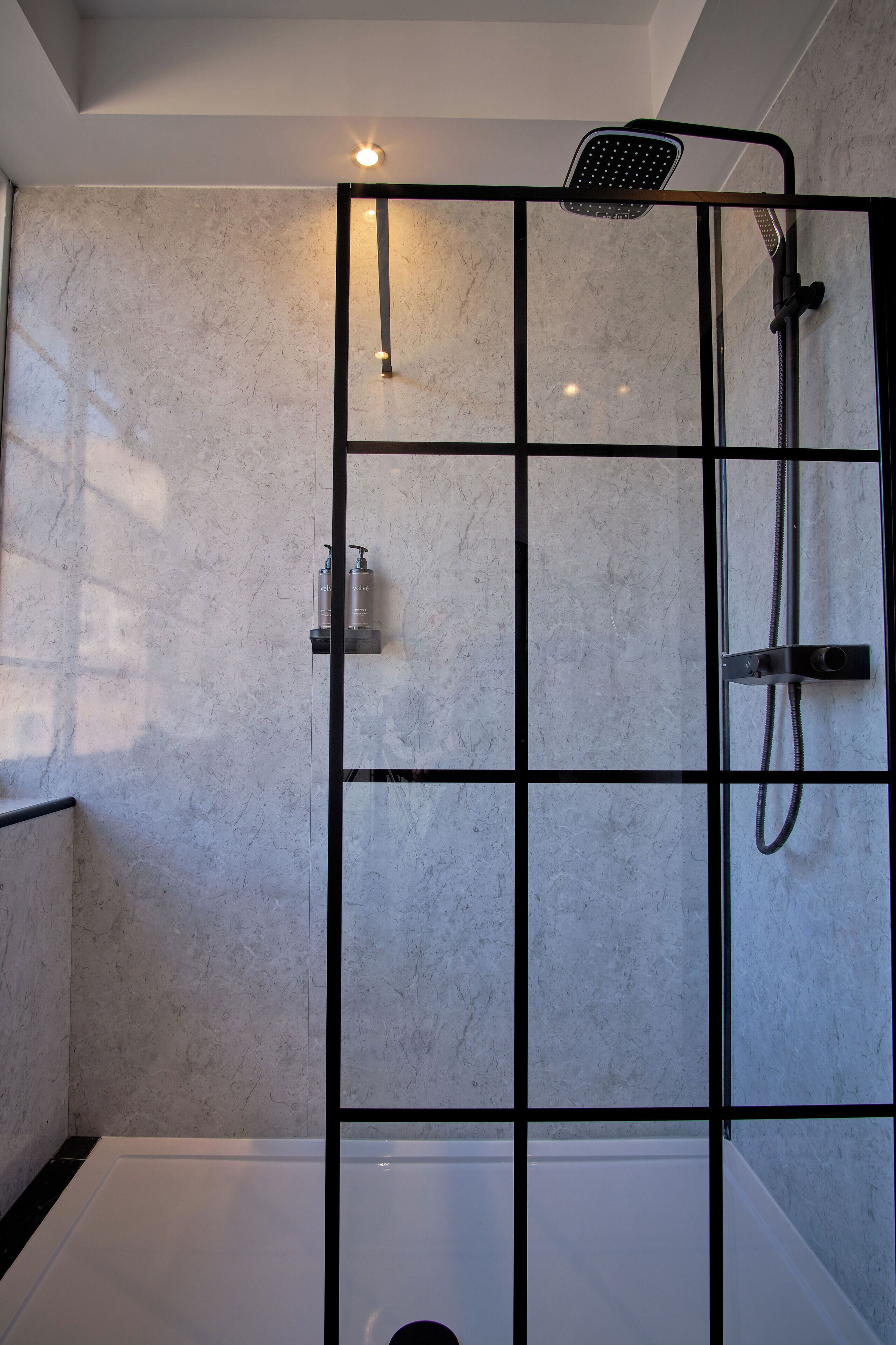 A modern shower enclosure with a glass partition, a handheld showerhead, and a handheld faucet.