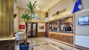 A reception area with a marble floor, a reception desk, a potted plant, and a television screen.