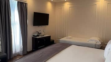 A modern hotel room with a large bed, a bedside table with a flat-screen TV, and a window with curtains.